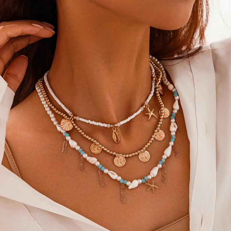Close-up of a woman wearing layered necklaces with gold coins, cowri shell and starfish charms.turquoises pearls.