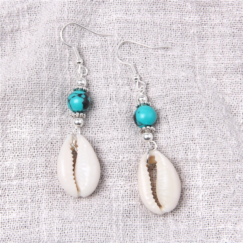 Pair of earrings with cowrie shells and turquoise beads on a textured fabric background