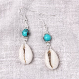 Pair of earrings with cowrie shells and turquoise beads on a textured fabric background