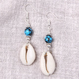 Pair of earrings with cowrie shells and blue beads on a textured fabric background