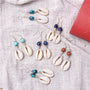 Cowrie shell earrings with colorful beads on a textured fabric background