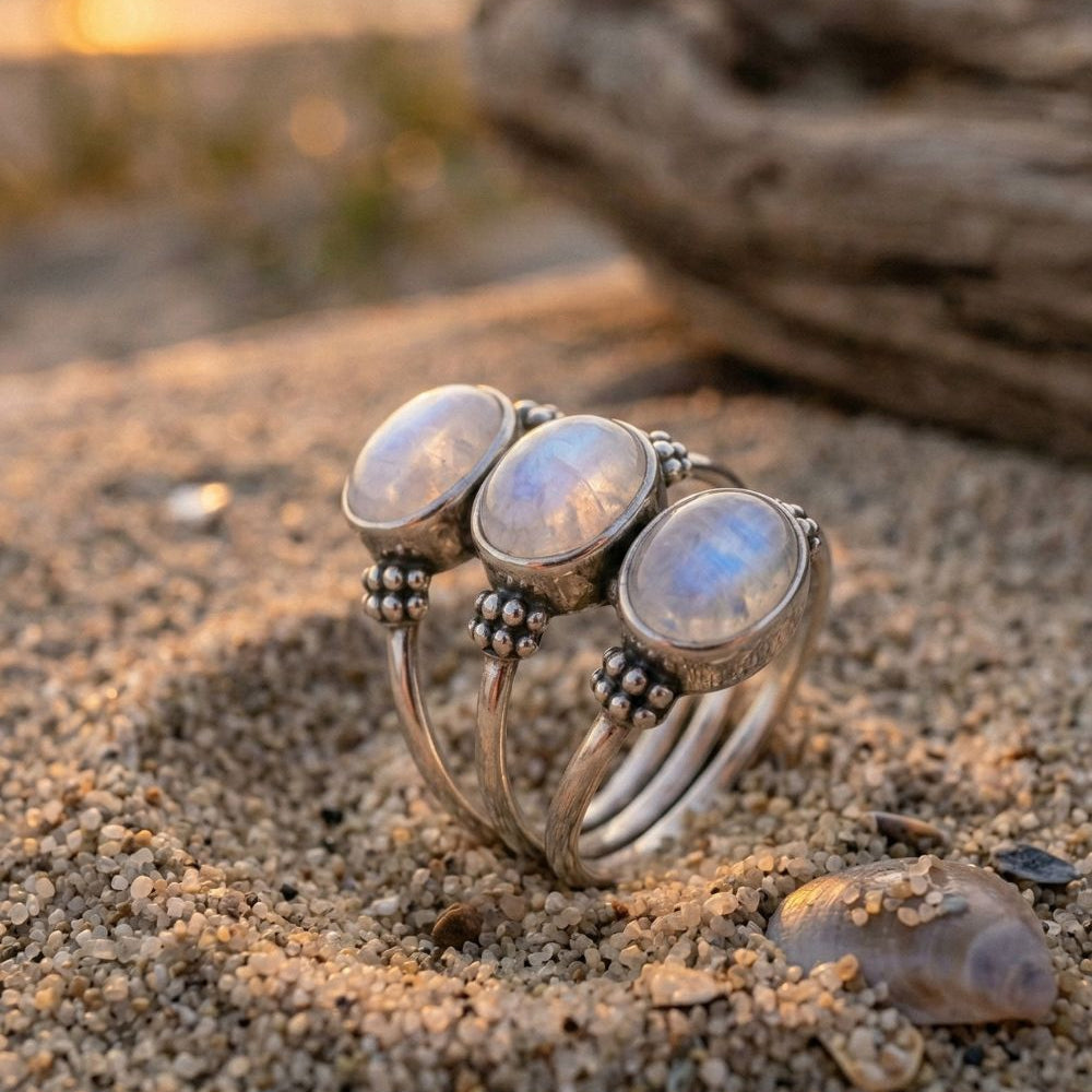 Silver ring with moonstone stones on a sandy beach with driftwood in the background
