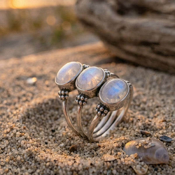 Silver ring with moonstone stones on a sandy beach with driftwood in the background