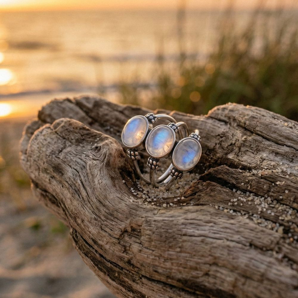 Three moonstone rings on a piece of driftwood with a sunset beach background