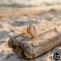 Gold ring with a cowrie shell on a piece of driftwood on a beach, featuring the 'Shell Vibe' brand.