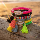 Colorful bracelets with tassels on a wooden log by the beach