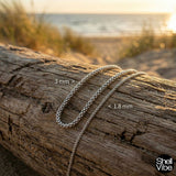 Sterling silver chain on a log with beach background, showing size comparison.