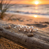 Sterling silver cowrie rings on a wooden log with a sunset over water in the background