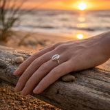Hand wearing a sterling silver cowrie shell ring on a beach with a sunset in the background
