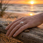 Hand wearing a sterling silver cowrie shell ring on a beach with a sunset in the background