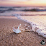 Sterling silver shell necklace on sand with ocean waves at sunset