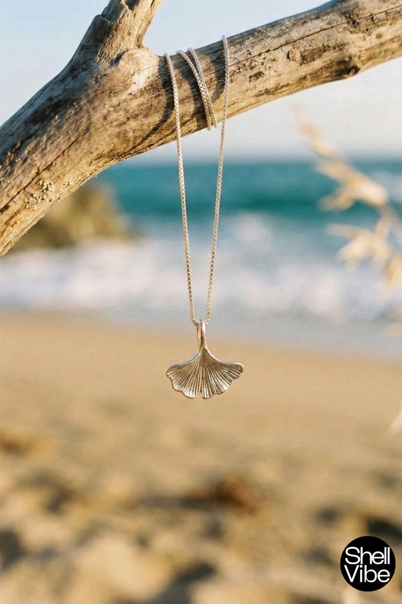Shell-shaped pendant on a chain hanging from a branch with a beach background