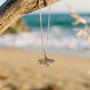 Shell-shaped pendant on a chain hanging from a branch with a beach background