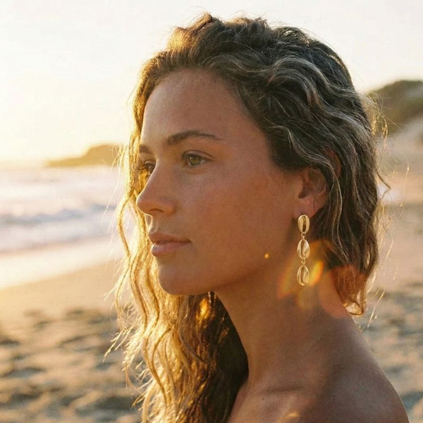 Woman with gold cowrie earrings on a beach at sunset