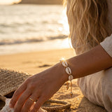 Woman sitting on a beach at sunset, wearing a cowrie shell bracelet.