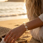 Woman sitting on a beach at sunset, wearing a cowrie shell bracelet.