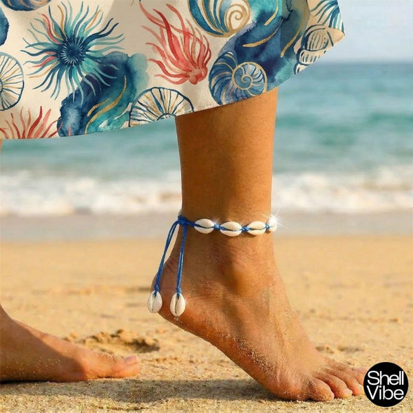 Person wearing a colorful skirt with cowrie shell anklets on a beach