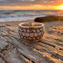 Decorative silver ring on a wooden plank with a sunset over water in the background