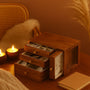 Walnut wooden jewelry box with open drawers displaying watches and gold accessories, placed on a warm-toned table with candles and pampas grass in a cozy boho interior.